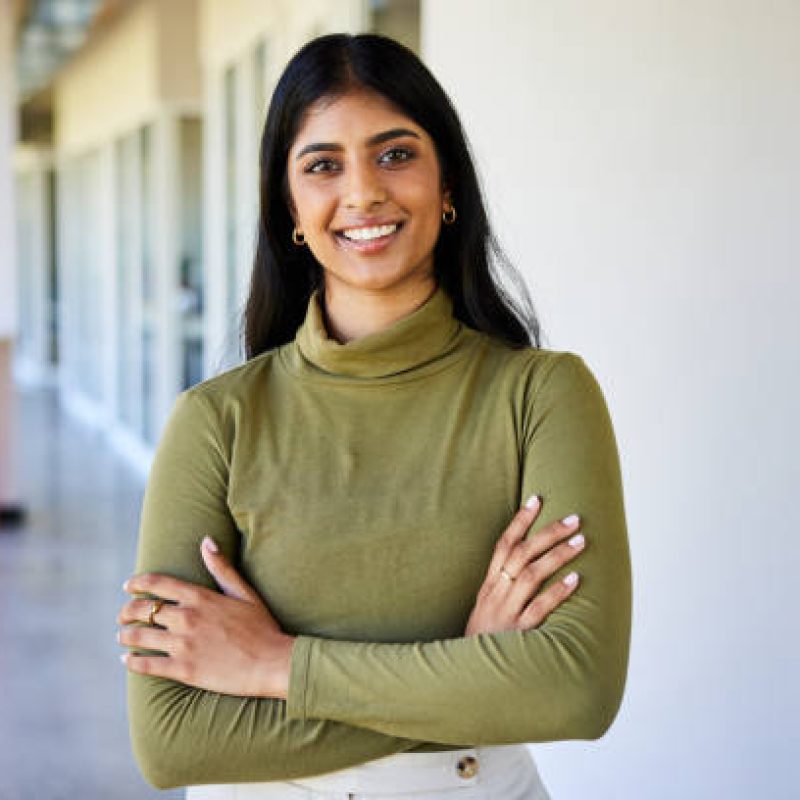 Portrait of a confident businesswoman smiling while standing with her arms crossed in the bright hallway of a modern office